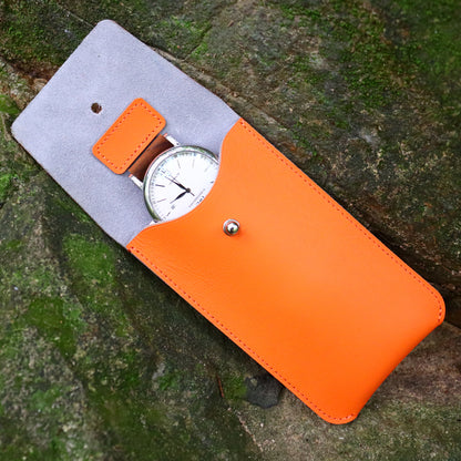 A high-contrast outdoor product shot featuring the open orange leather watch pouch resting diagonally on a rugged, damp moss-covered stone. An elegant white-dial luxury timepiece sits securely inside, perfectly demonstrating an outdoor-proof, shock-absorbing storage solution for watch enthusiasts who hike or camp.